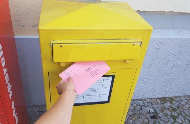 Eine Hand steckt einen Wahlbrief in einen Briefkasten.