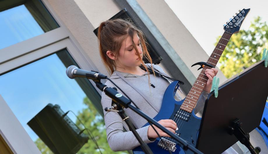 Eine Jugendliche spielt E-Gitarre auf der Terassenbühne der Städtischen Musikschule Potsdam. Es ist sommerlich bunt.