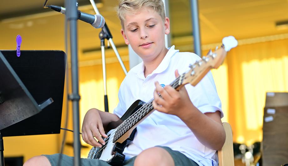 Ein Junge spielt E-Bass auf der Terassenbühne der Städtischen Musikschule Potsdam. Es ist sommerlich bunt.