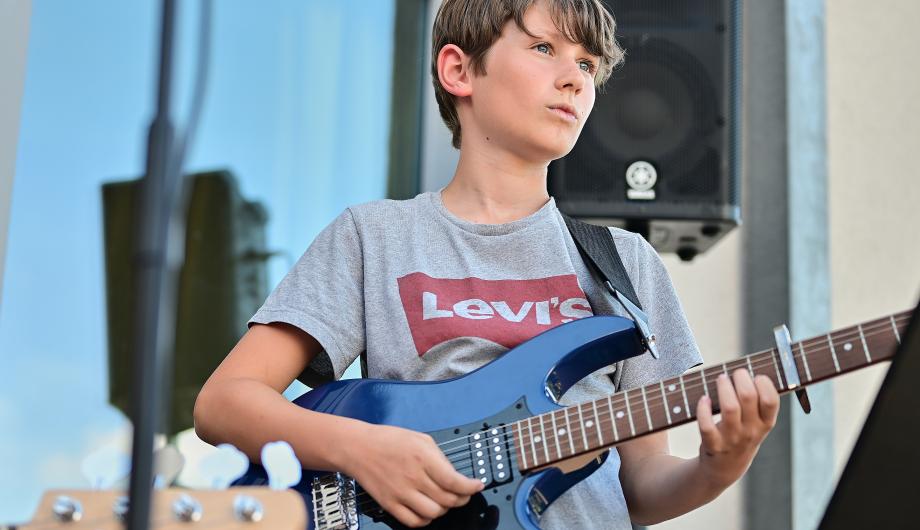Ein junge spielt E-Gitarre auf der Terassenbühne der Städtischen Musikschule Potsdam. Es ist sommerlich bunt.