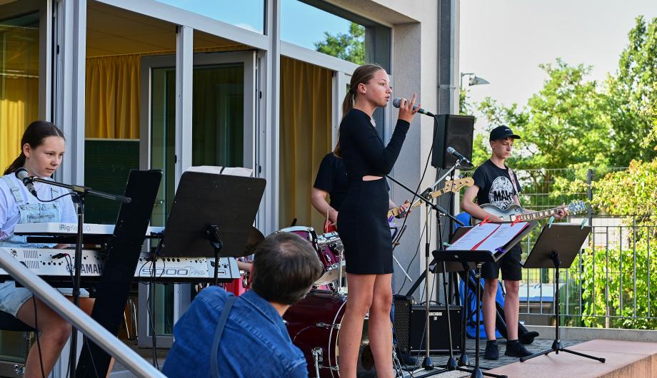 Auf einer Terassenbühne der Städtischen Musikschule Am Stern spielt eine Band mit Sängerin bei sommerlichem Wetter