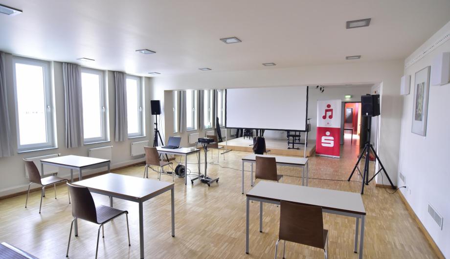 Tische, Stühle und eine BEamerleinwand sind für eine Hybridveranstaltung des Wettbewerbes Jugend Musiziert in einem Raum der Musikschule am Campus am Stern aufgebaut.