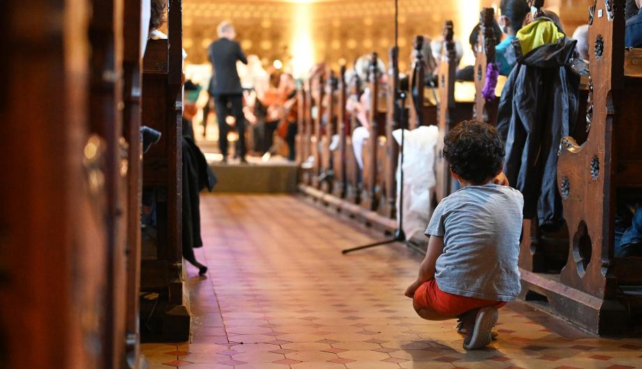 Ein Junge hockt im Gang zwischen den Sitzreihen der Erlöserkirche in Potsdam. Er ist fasziniert vom Klang des Jugendsiinfonieorchesters, das im Hintergrund nur unscharf zu sehen ist