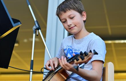Ein Junge zupft die elektrische Bassukulele auf einer Außenbühne der Städtischen Musikschule Am Stern