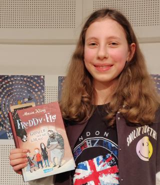 Auf dem Foto ist Enna Marwan aus der Karl-Foerster-Grundschule. Sie hält in der Hand das Buch „Freddy und Flo gruseln sich vor nix!“
