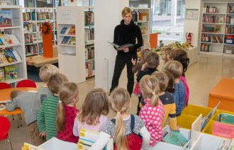 Das Foto zeigt einer Vorleserin aufmerksam lauschende Kinder in der Stadt- und Landesbibliothek.