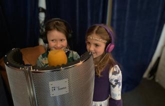 Zwei kleine Mädchen froh lächelnd in einer kleinen mobilen Aufnahmekabine mit Mikrophonen