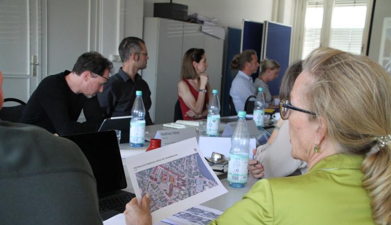 Zu sehen sind mehrere Mitglieder des Gestaltungsrates bei einer Sitzung, die sich Pläne ansehen.
