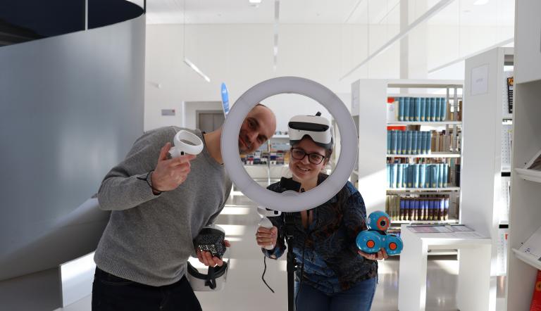 Zwei Mitarbeitende der SLB tragen VR-Brillen und schauen durch einen Beleuchtungsring.