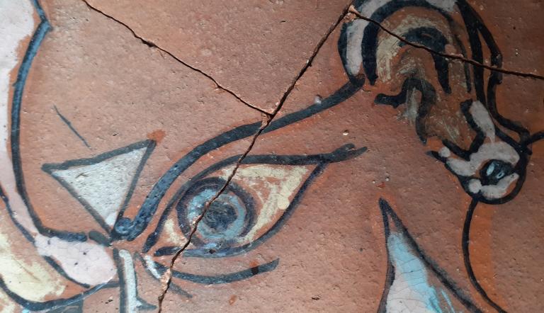 Das Foto zeigt einen Teil einer bemalten Keramik. Zu sehen sind unter anderem ein gezeichnetes Auge und ein Ohr.