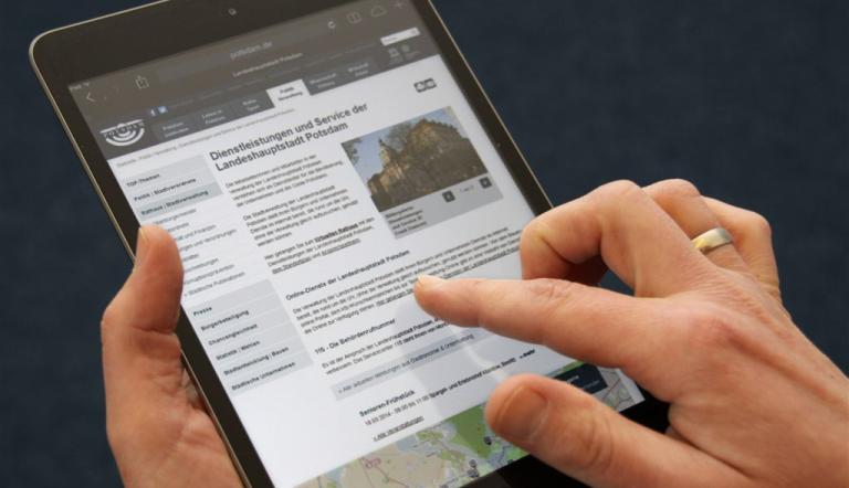 Das Foto zeigt ein Tablet mit einer Unterseite von potsdam.de und eine Hand, die darauf navigiert.