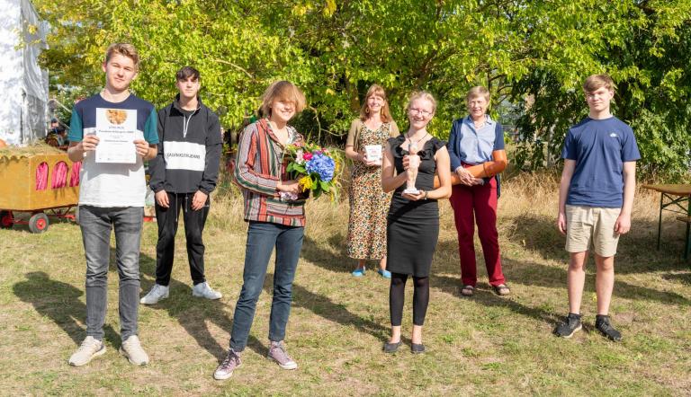 Lehrerin, Schülerinnen und Schüler der Waldorfschule Potsdam halten Blumen, Urkunde und Klimapreisskulptur in den Händen
