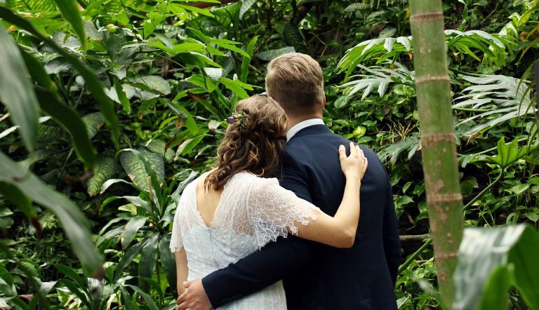 Auf dem Foto ist ein sich umarmendes Hochzeitspaar in der Tropenwelt der Biosphäre zu sehen.