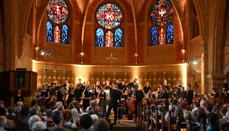 Vor der golden anmutenden Kulisse der Erlöserkirche erhebt sich das Jugendsinfonieorchester der Städtischen Musikschule Potsdam zum verdienten Applaus.